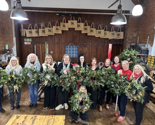 A festive Christmas wreath-making workshop in Cheshire with a group of colleagues creating handmade wreaths, enjoying afternoon tea, and celebrating together.