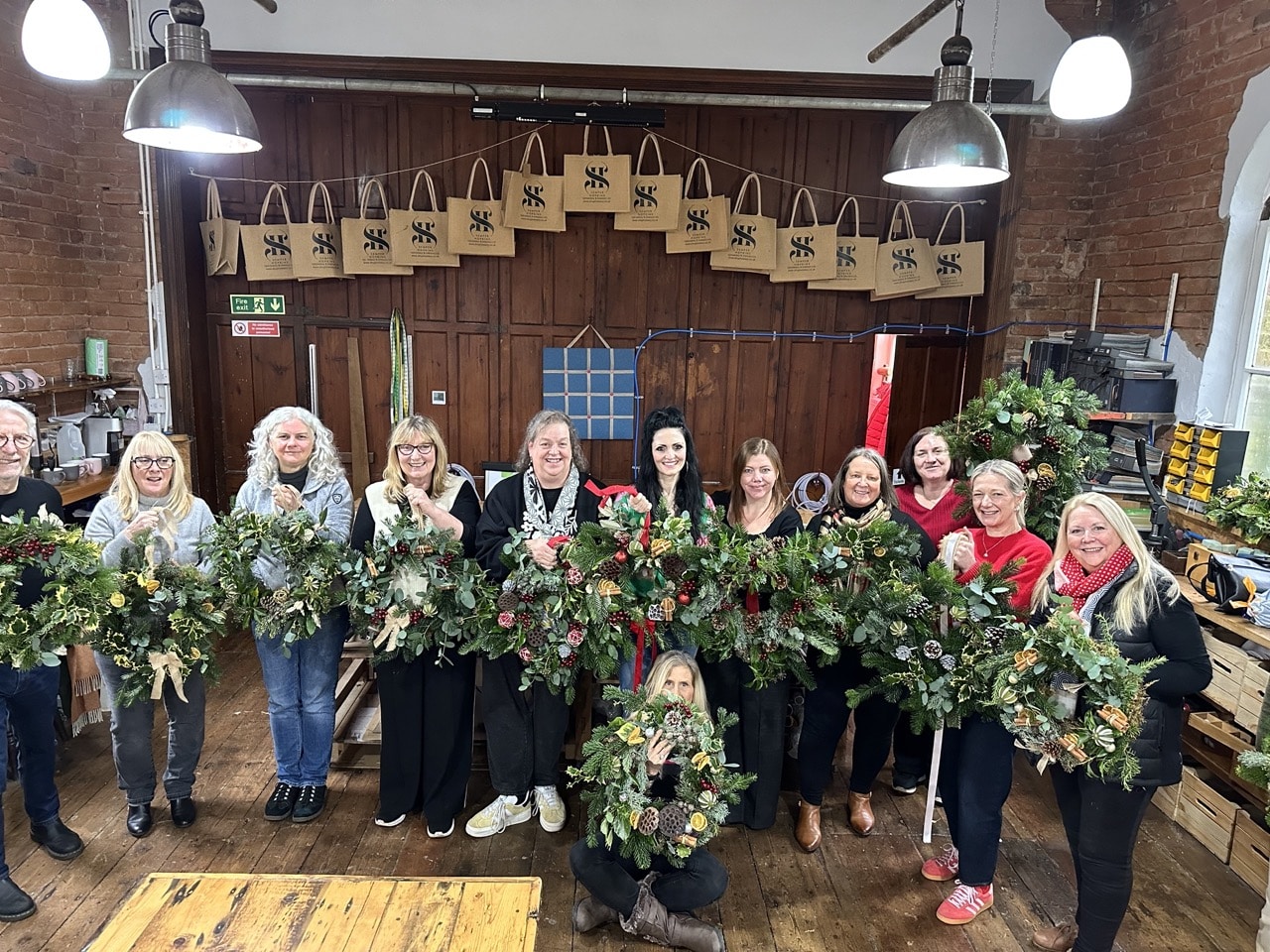 A festive Christmas wreath-making workshop in Cheshire with a group of colleagues creating handmade wreaths, enjoying afternoon tea, and celebrating together.