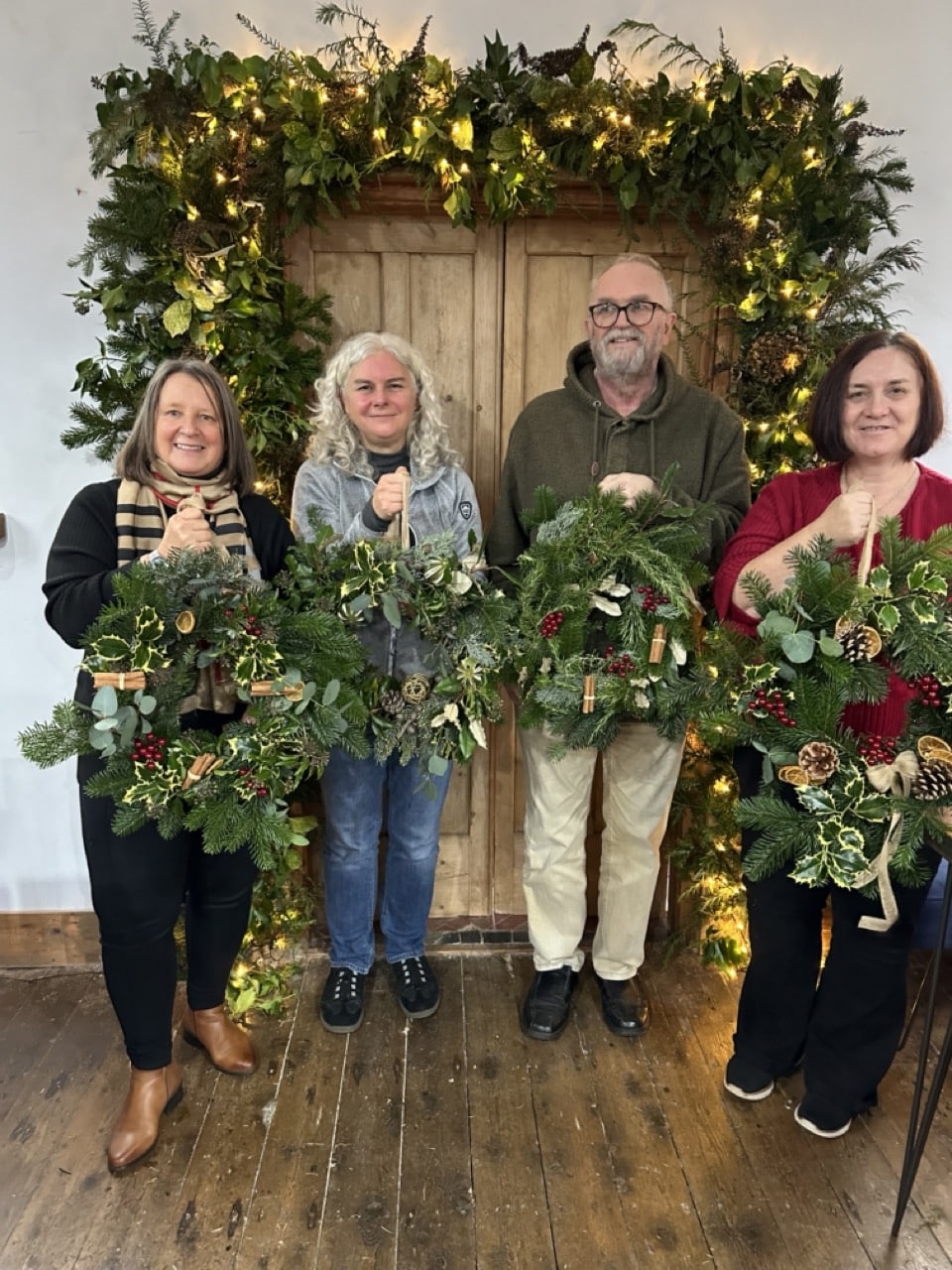 Participants proudly holding up their finished Christmas wreaths after a festive team workshop.