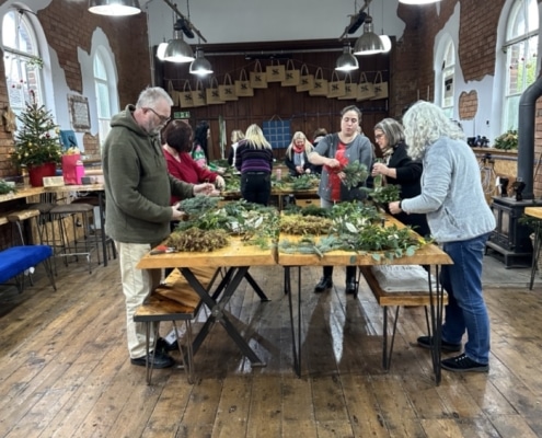 Mixed group of men and women smiling while working on handmade wreaths at a corporate Christmas workshop.