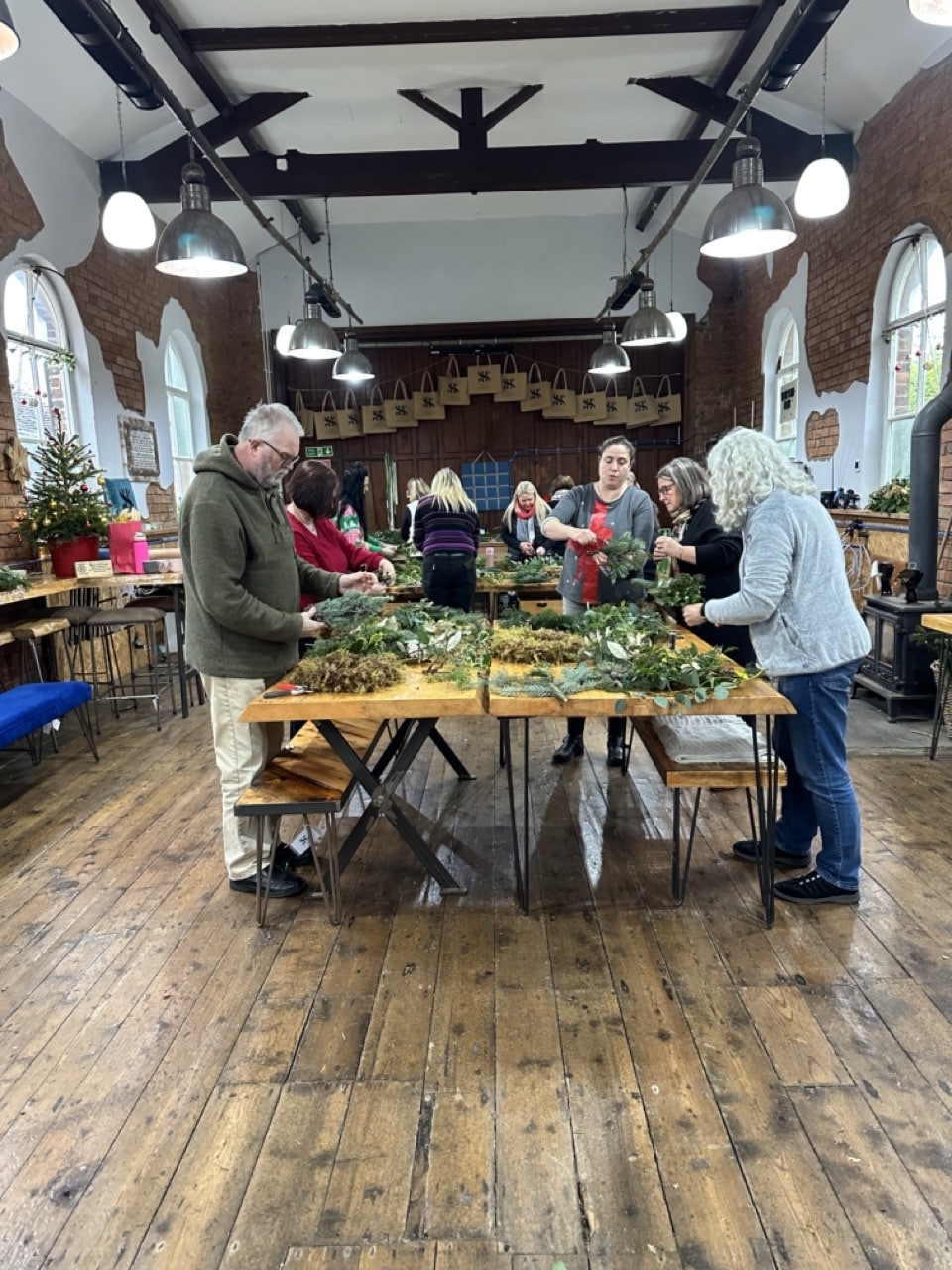 Mixed group of men and women smiling while working on handmade wreaths at a corporate Christmas workshop.