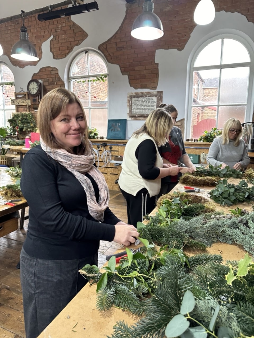 Close-up of hands arranging festive foliage, pinecones, and ribbon during a Christmas wreath-making workshop.