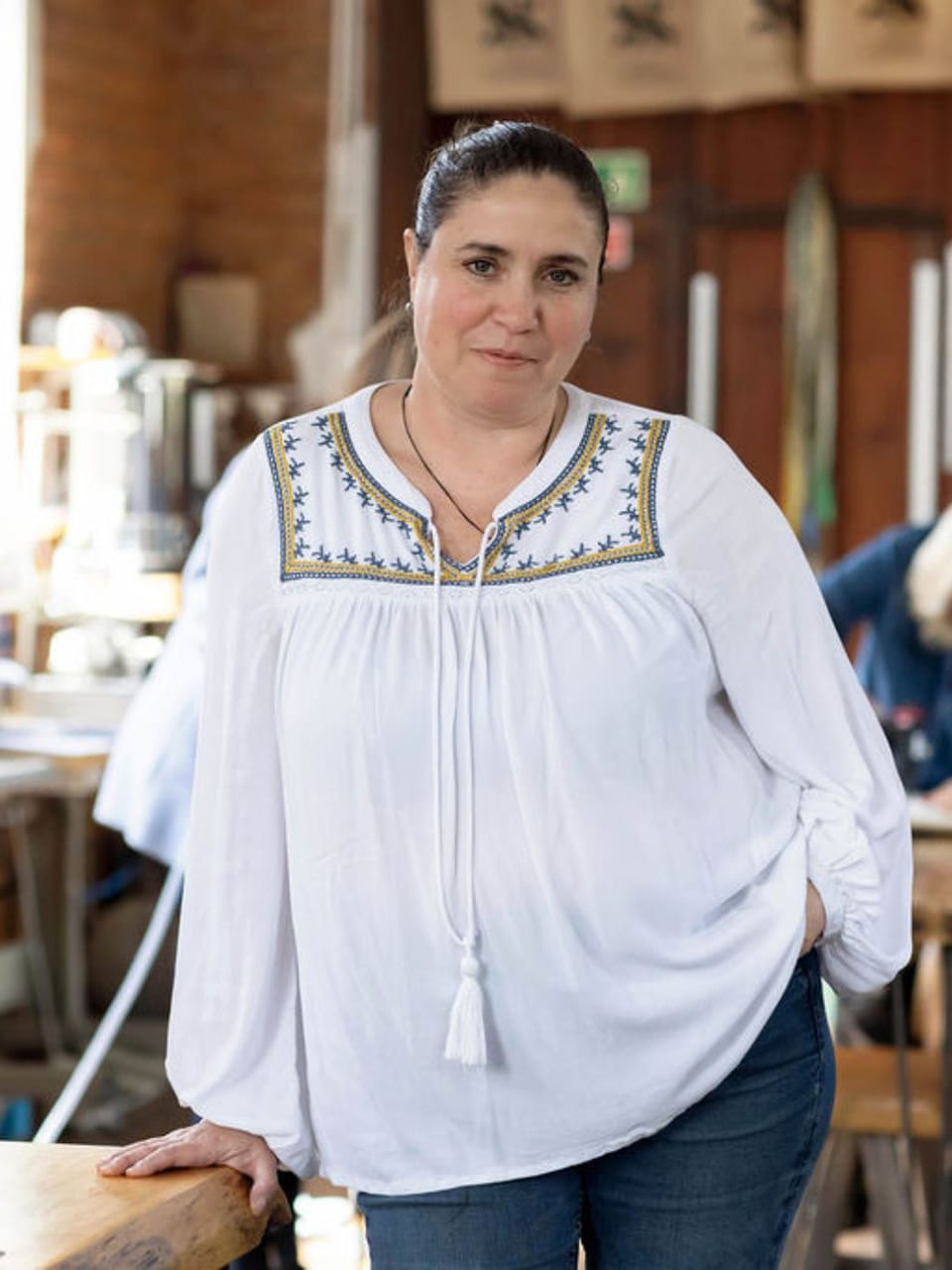 ros-creative-workshop-portrait Ros smiling inside the chapel, wearing a white embroidered blouse, standing in the creative workshop space.